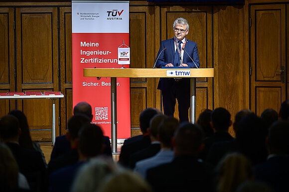 Mann im Anzug hält Rede auf Bühne.