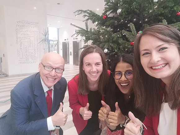 Drei Damen und ein Herr vor einem Weihnachtsbaum. Alle halten ihre Daumen nach oben.