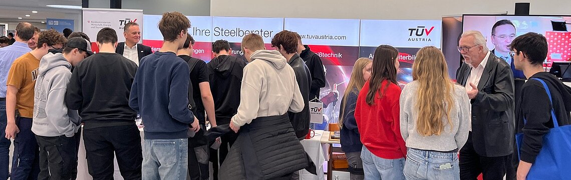 TÜV AUSTRIA Infostand. Im Vordergrund viele interessierte Jugendliche.