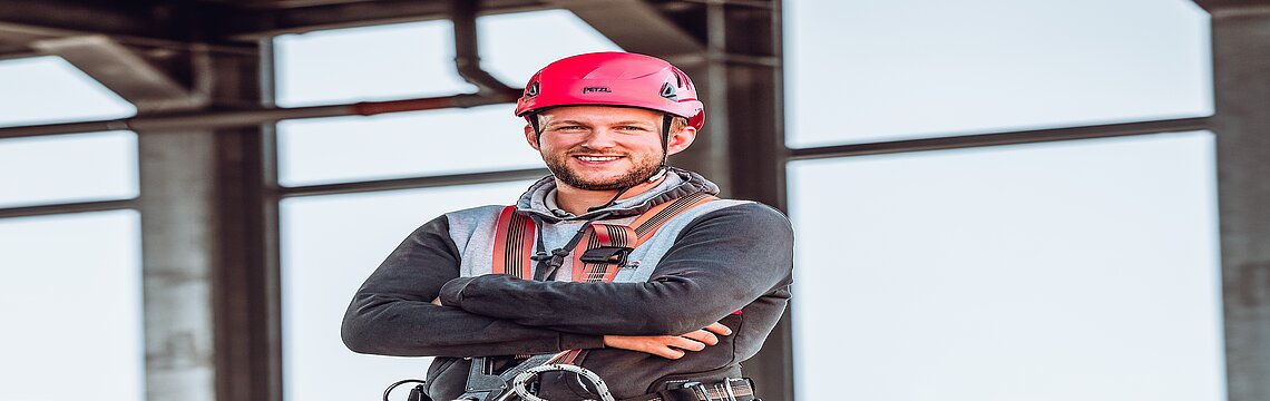 Ein Mann in persönlicher Schutzausrüstung steht vor einem Bauwerk.