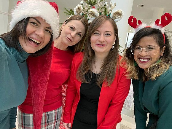 Vier Frauen in festlichen roten und grünen Outfits posieren fröhlich für ein gemeinsames Bild.