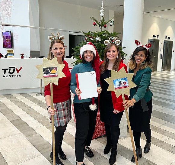 Drei Frauen in Weihnachtsoutfits halten stolz ein Zertifikat in die Höhe.