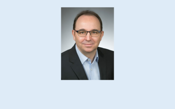 Ein Mann mit Brille und Anzug steht für ein Foto bereit.