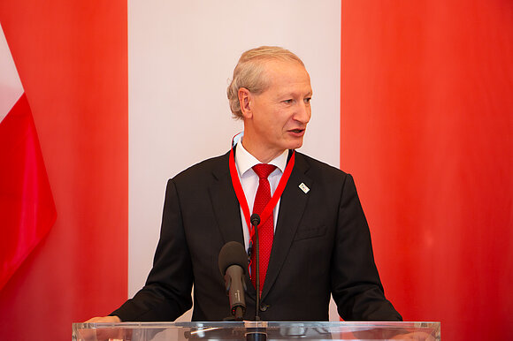 Mann im Anzug hinter einem Rednerpult. Im Hintergrund die Österreich-Flagge.