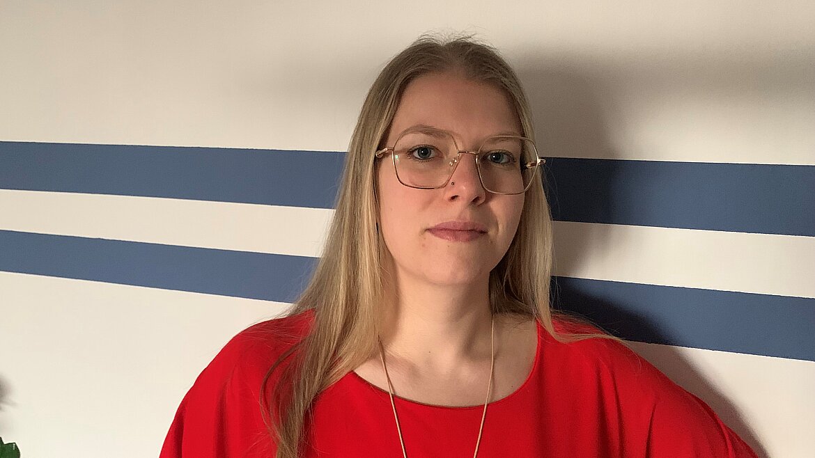 Eine Frau mit Brille trägt ein rotes Hemd und blickt freundlich in die Kamera.