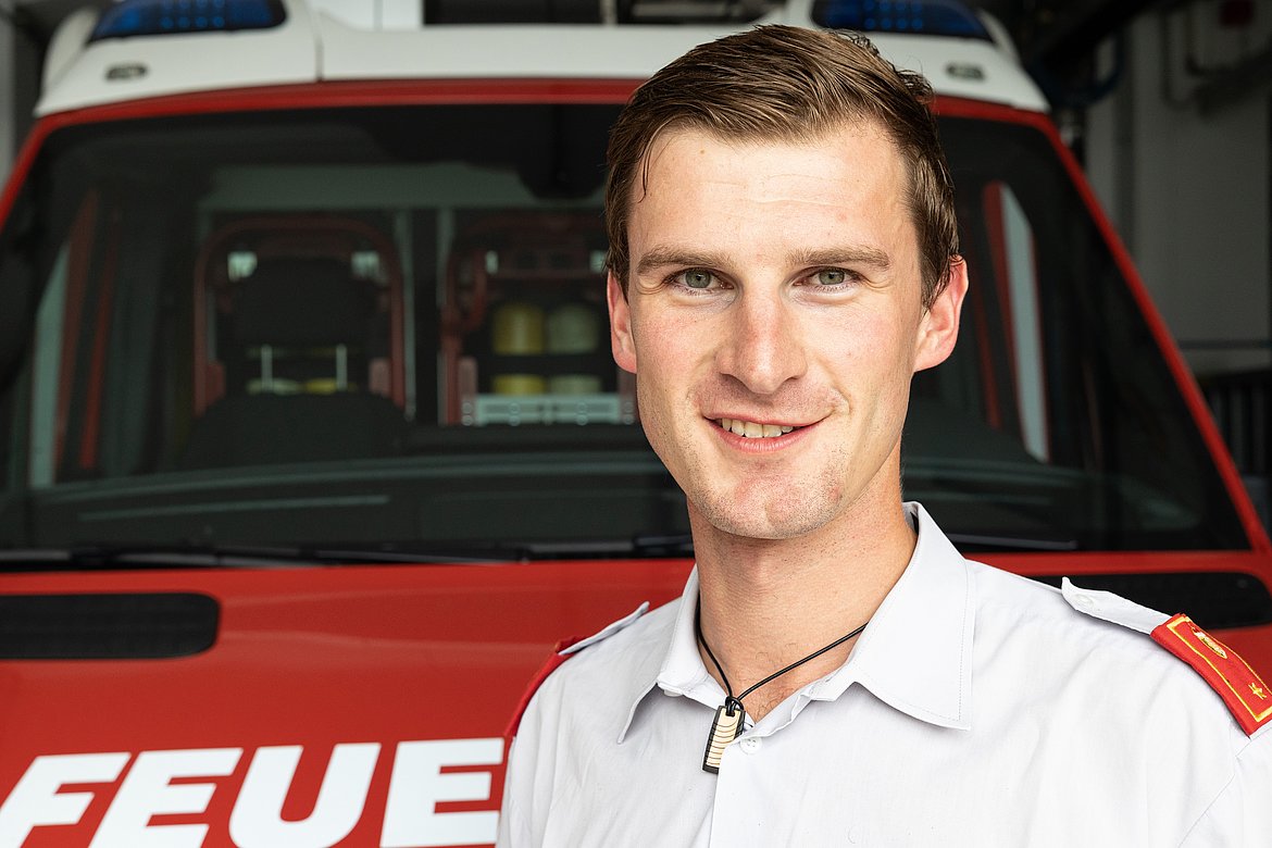 Ein Mann in einem weißen Uniformhemd steht vor einem Feuerwehrauto und blickt aufmerksam in die Kamera.