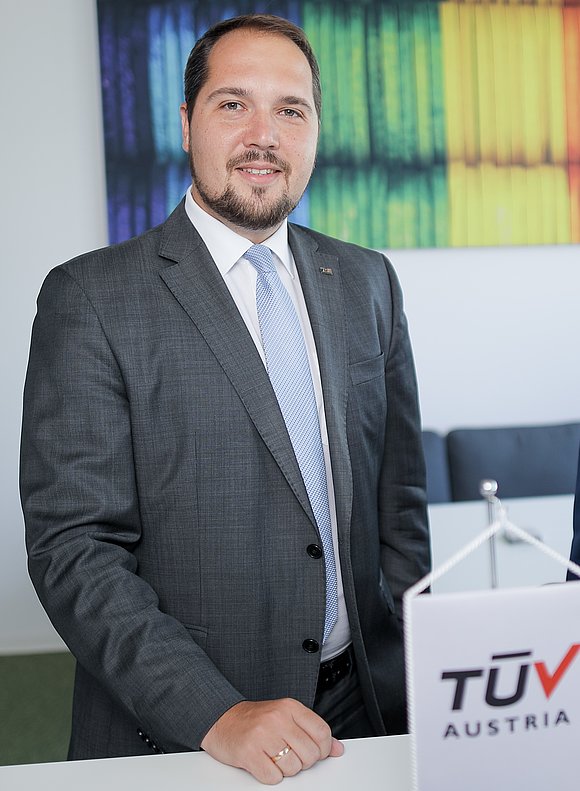 Ein Mann in Anzug steht neben einem Tisch mit einem TÜV-Schild.