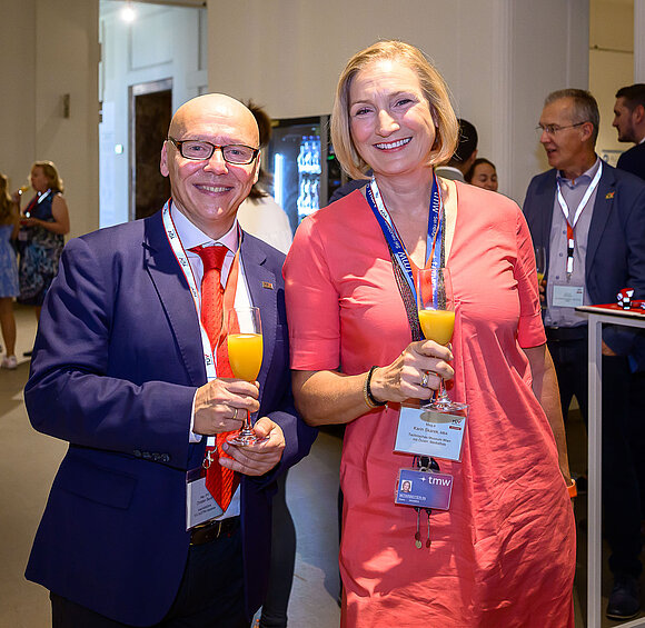Herr und Dame lächeln und halten Sektgläser mit Orangensaft in den Händen.