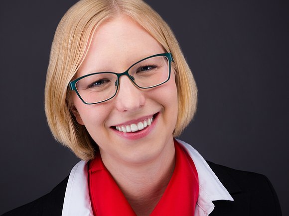 Eine Frau mit Brille und rotem Schal, die freundlich in die Kamera lächelt.