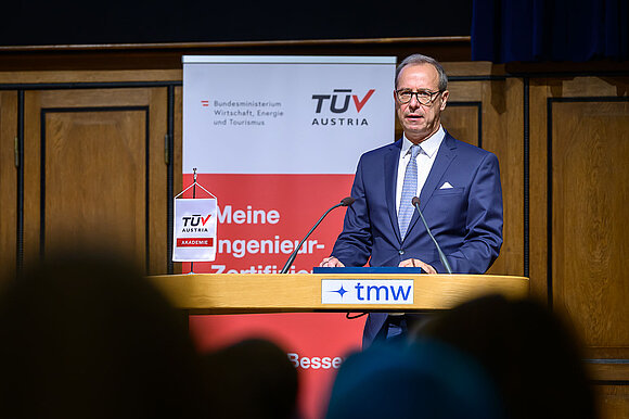 Mann im Anzug hält Rede auf Bühne.