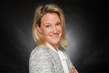 Eine Frau mit blonden Haaren trägt ein weißes Hemd und blickt freundlich in die Kamera.