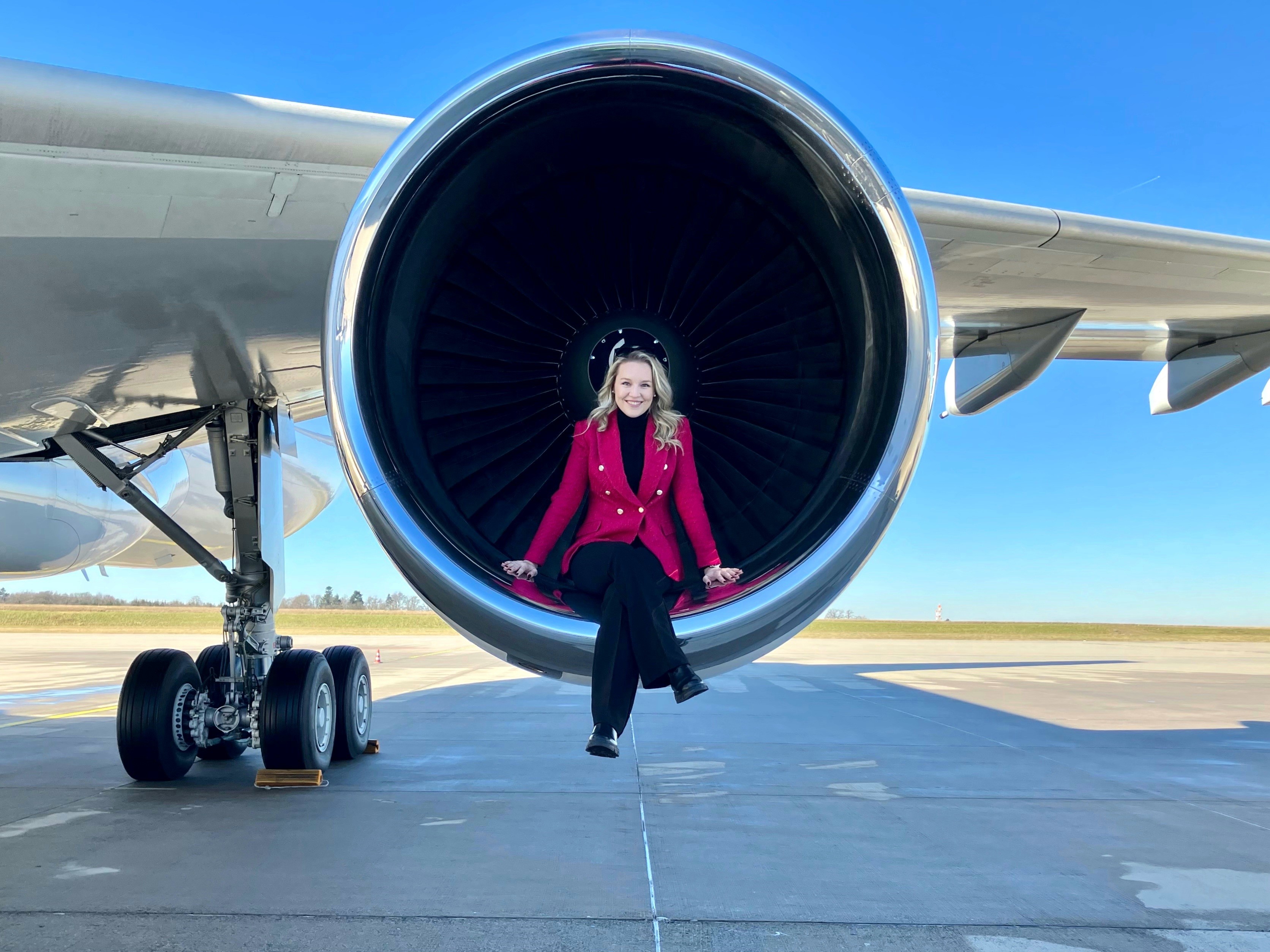 Eine Frau sitzt auf dem Triebwerk eines Flugzeugs und strahlt Selbstbewusstsein und Unkonventionalität aus.