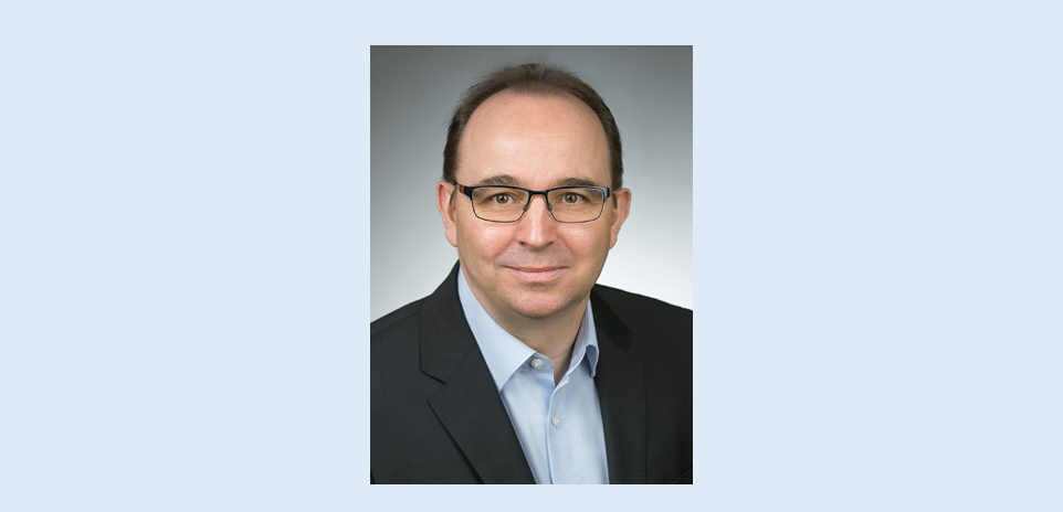 Ein Mann mit Brille und Anzug steht für ein Foto bereit.